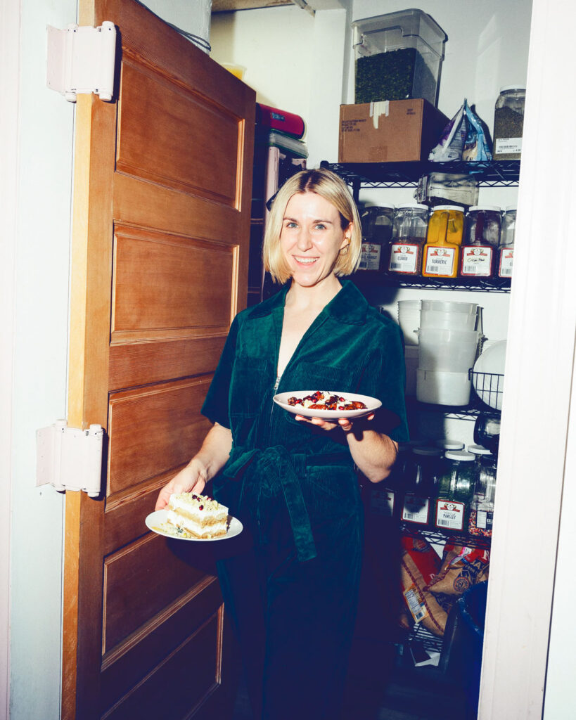 Food influencer Justine Doiron stands in the doorway of a pantry holding two plates of food