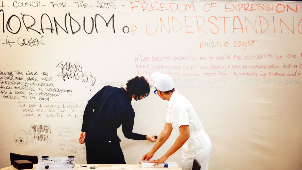 Two people writing on a white canvas for the work "Memorandum of Understanding"