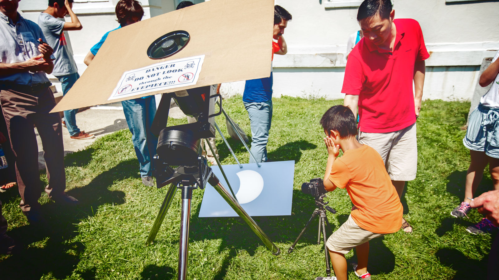 A man and child looking at the eclipse shadow from a large pinhole camera
