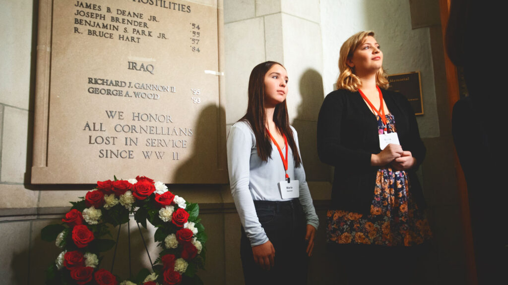 Maria Gannon, left, and Maria Wood stand beside the war memorial plaque in the Anabel Taylor Hall rotunda that honors their fathers, Maj. Richard J. Gannon II ’95 and Capt. George A. Wood ’93, two alumni killed during the conflict in Iraq.