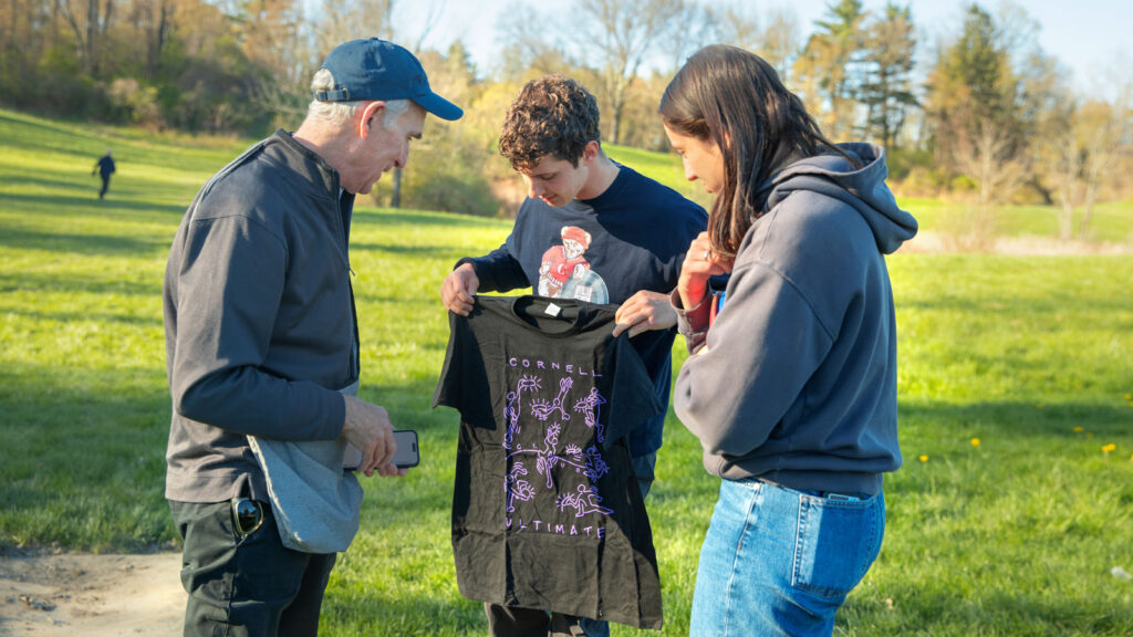 Tomer Poole-Dayan ’24, center, of the Cornell Buds Ultimate team, presents an Ultimate T-shirt to Bill Nye ’77, left, as Eve Lesburg ’25 of the Cornell women’s Ultimate team the Wild Roses looks on