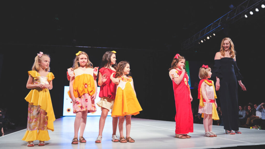 Julia DeNey and six child models walk on the runway.