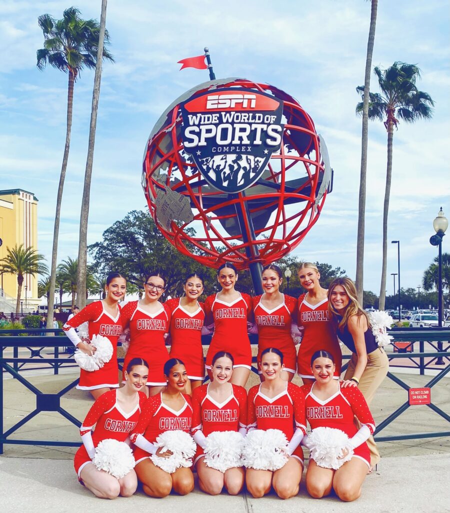The Cornell University Dance Team and Coach Amanda Hernandez smile in front of the ESPN Wide World of Sports Complex sign.