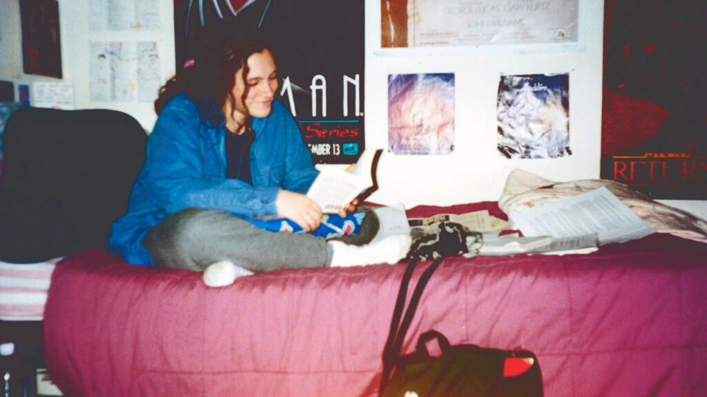 Michelle Knudsen sitting on her bed reading a book in her dorm room as a student