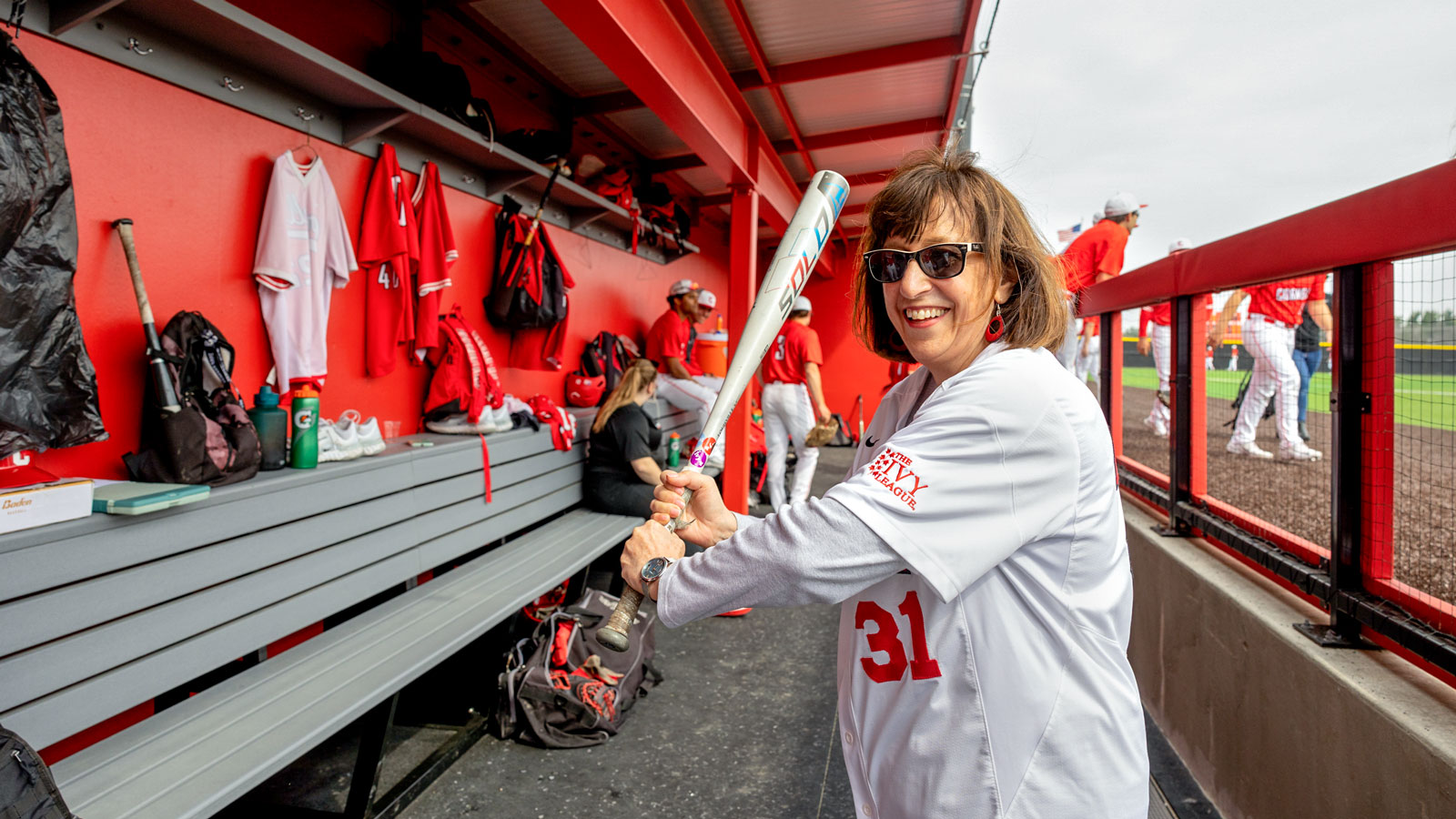 President Martha Pollack holds a baseball bat in the dugout at the new Booth Field in 2023