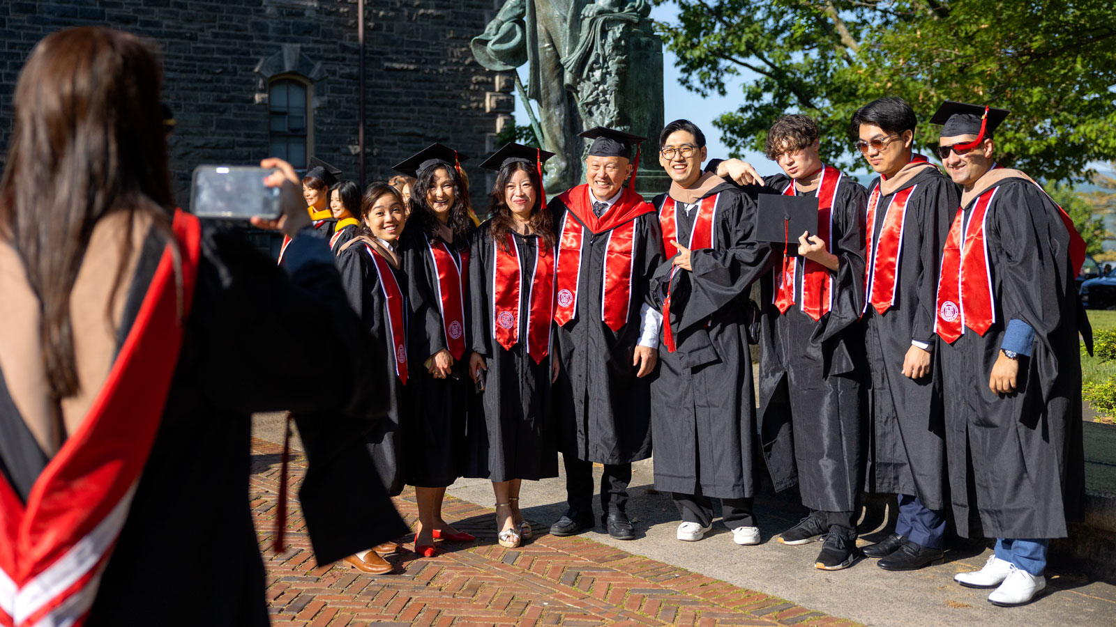 Graduates and new degree holders pose for a group photo near the Ezra Cornell statue on the Arts Quad during Commencement 2024 events