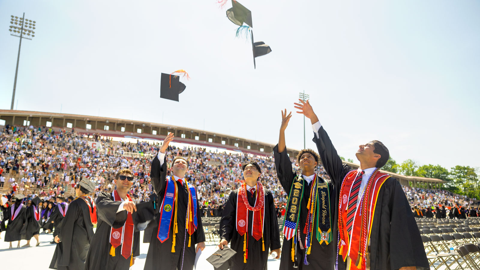 Graduates celebrate and toss their caps in the air in Schoellkopf Stadium during Commencement 2024 ceremonies