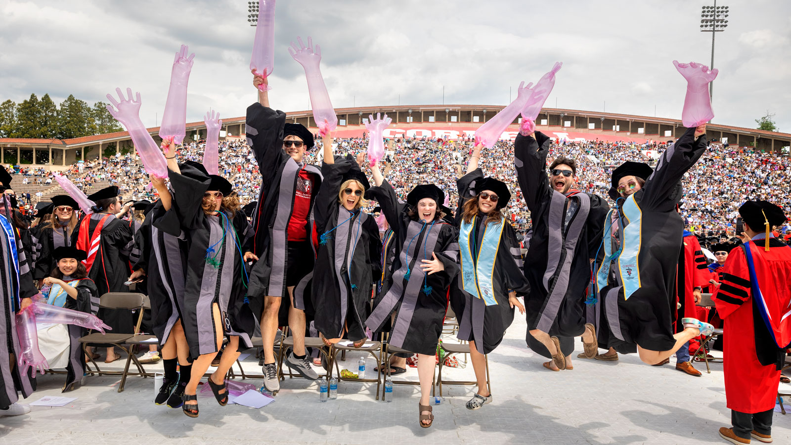 Graduating College of Veterinary Medicine graduates, inflated exam gloves in hand, jump in the air during Commencement 2024 ceremonies in Schoellkopf Stadium