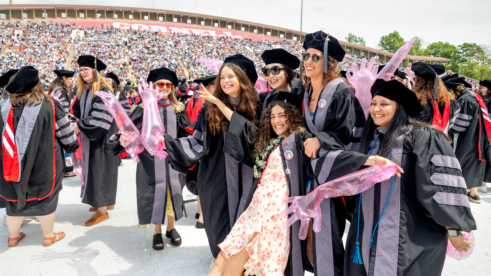 Graduating College of Veterinary Medicine graduates pose with inflated exam gloves during Commencement 2024 ceremonies in Schoellkopf Stadium