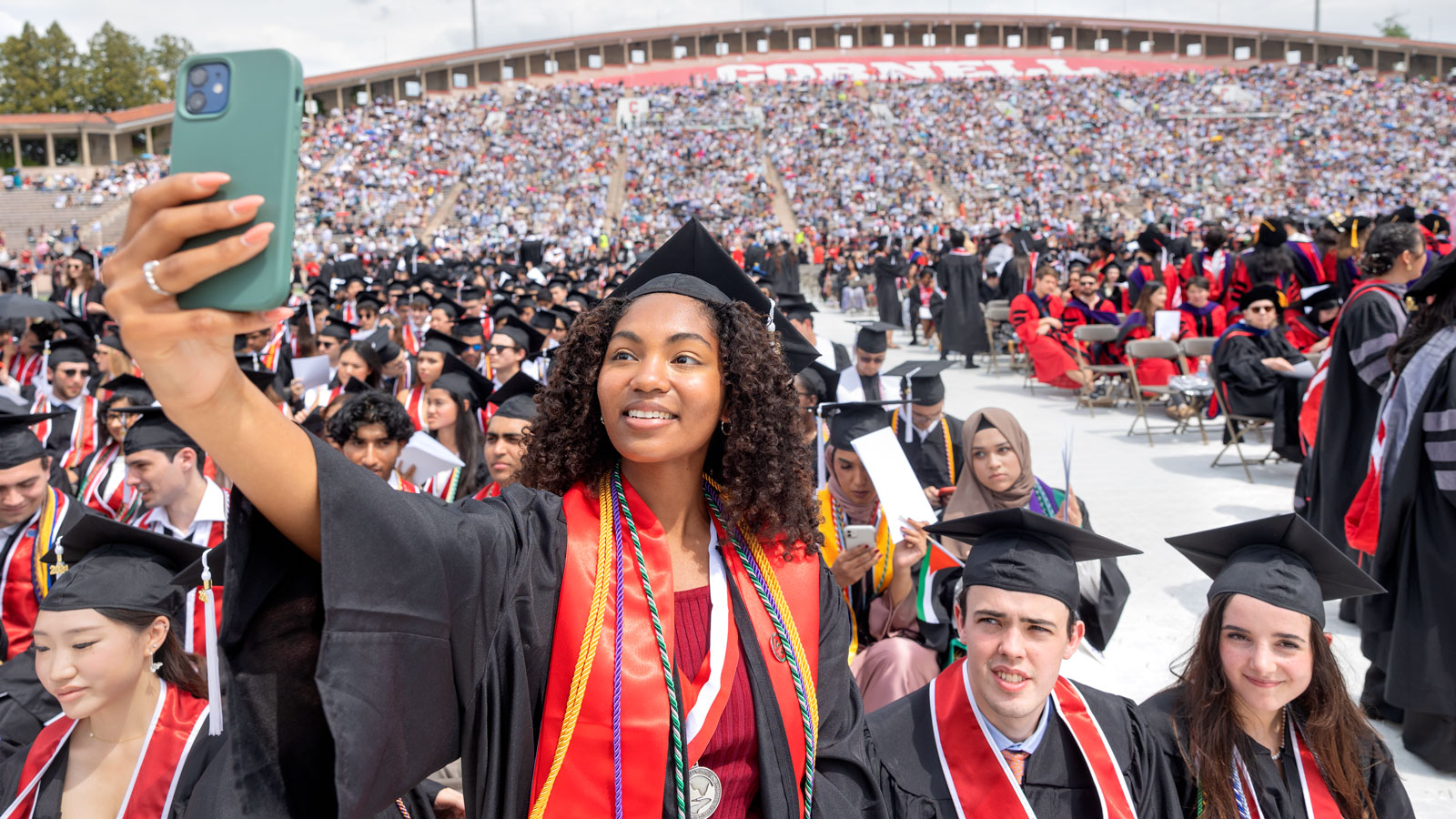 A Cornell graduate takes a selfie during Commencement 2024 ceremonies in Schoellkopf Stadium