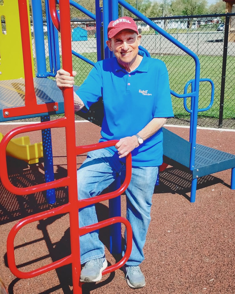 Richard Hagelberg smiles for a photo while standing on one of his colorful playgrounds