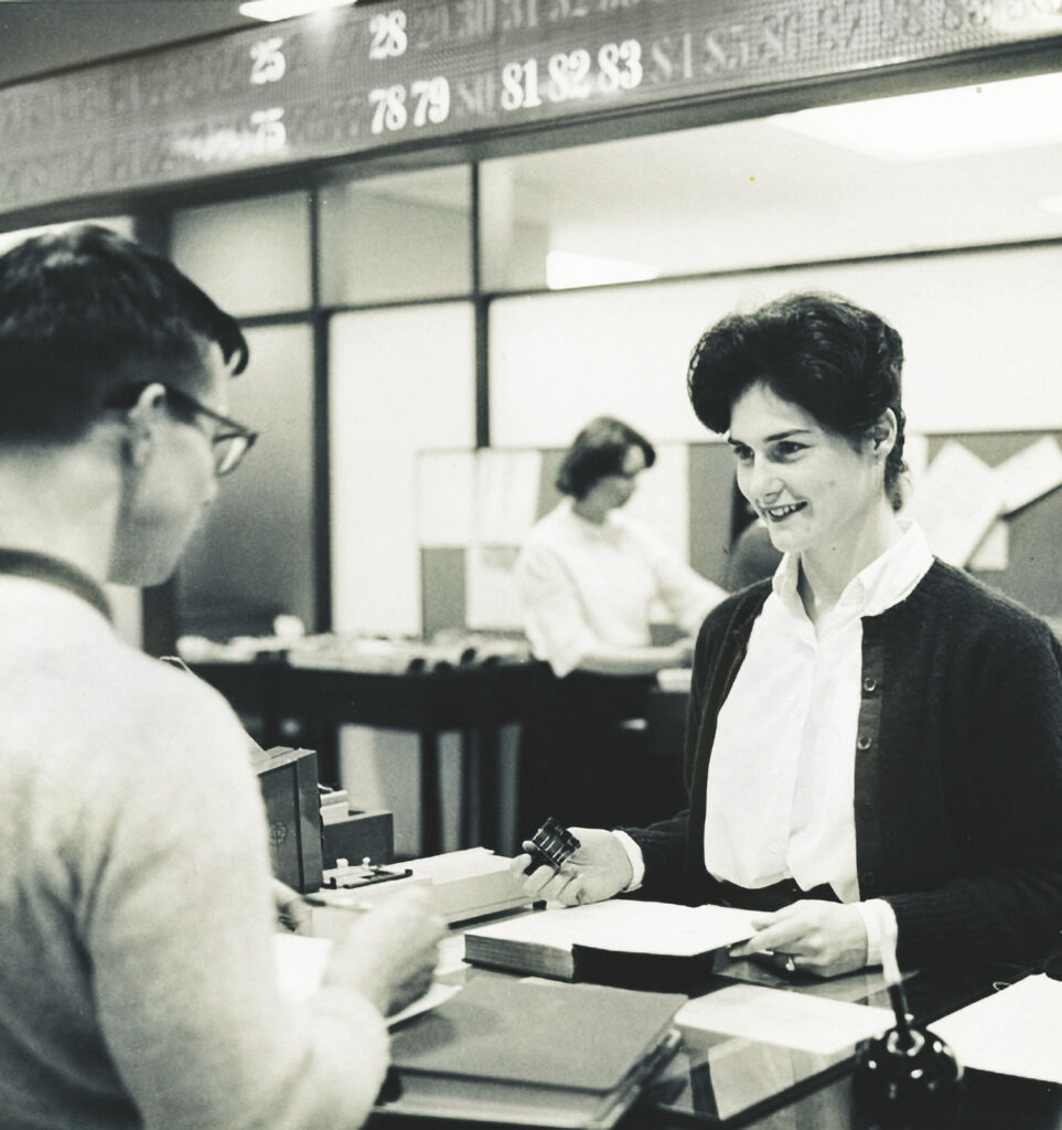 Archival photo shows Patricia Kelly ’63 checking out books in her role as a weekend student assistant at Olin Library