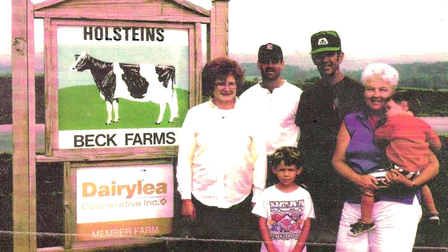 The Beck family stands in front of a sign on the farm