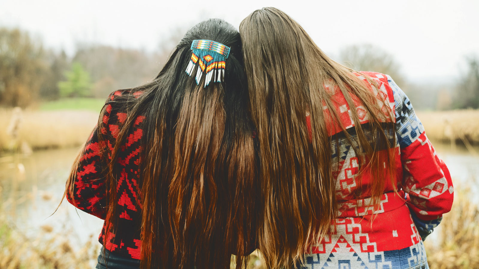 Two Native American woman with long hair lean on each other