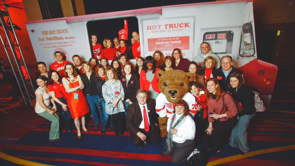 Cornell staff, alumni, and Touchdown the Bear posing in front of a Hot Truck mockup at the Cornell Alumni Leadership Council in Washington, D.C., 2012