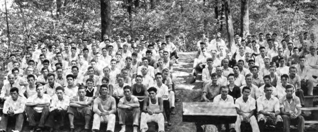 A group of dozens of men in white shirts sitting on benches during Cornell's 1933 Freshman Camp