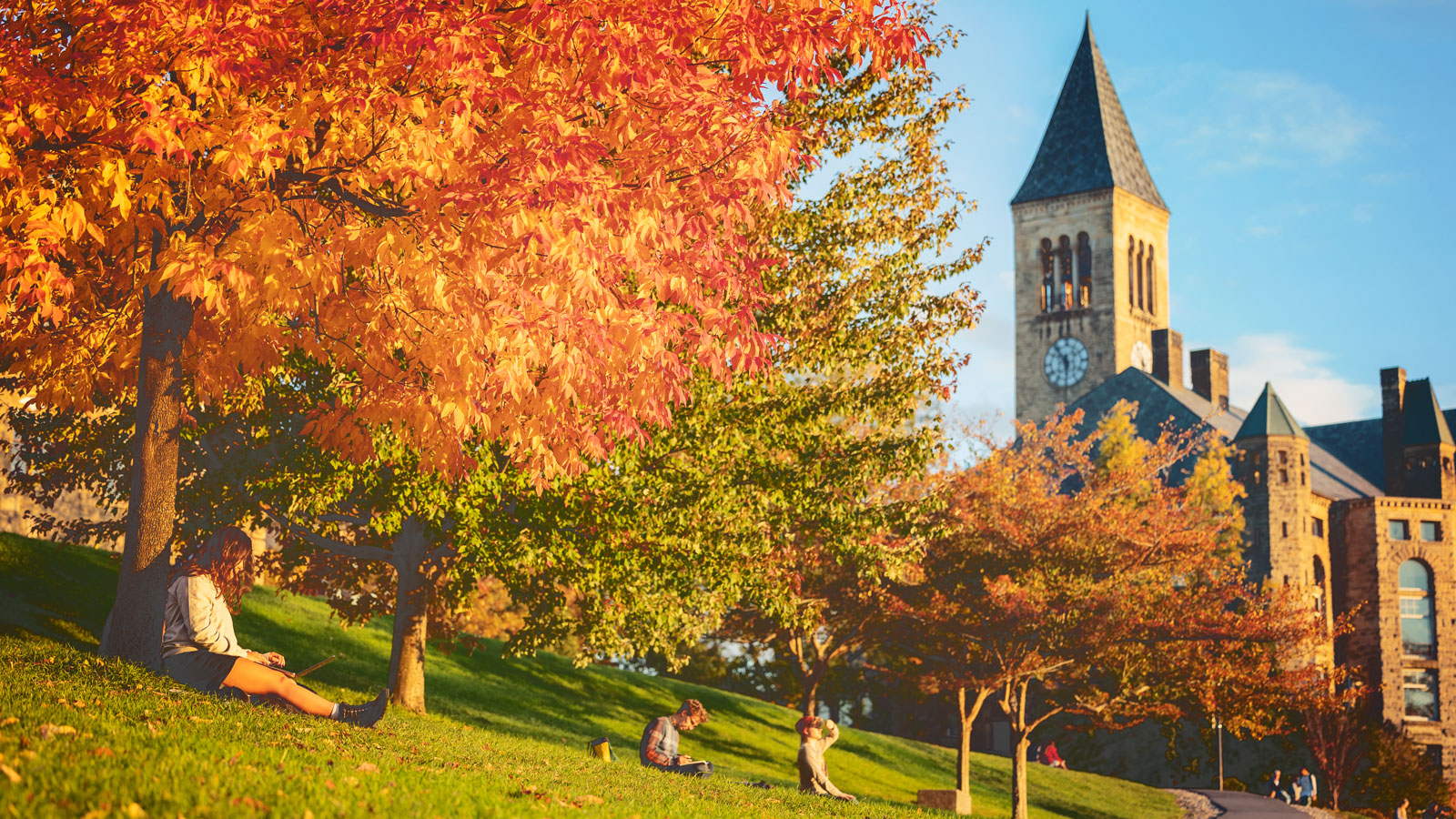 Students work, hang out, and take in the sunset from the top of Libe Slope in autumn, with McGraw Tower in the background.