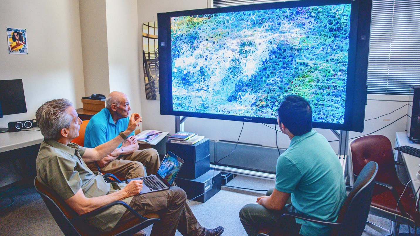 Daniel Ambrosi, along with professors Don Greenberg and Alex Kwan, look at one of his artworks on a big screen in Rhodes Hall