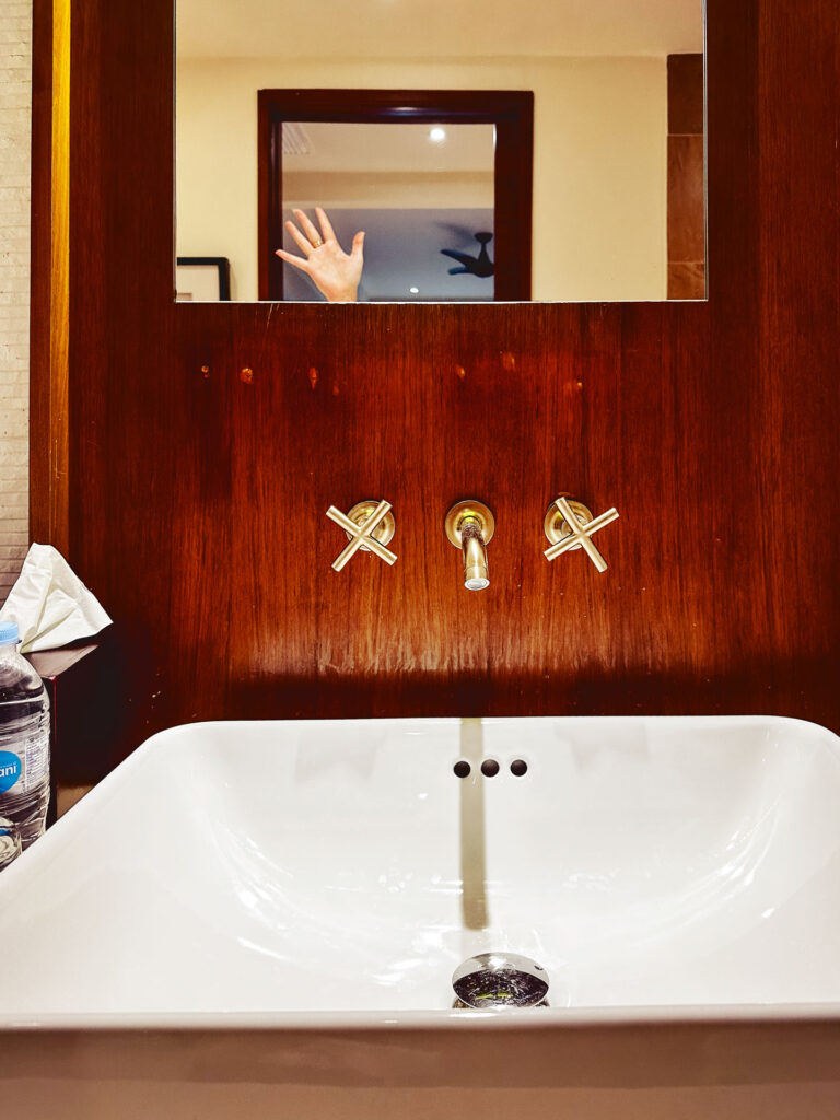 A hand waving, seen in a mirror above a sink