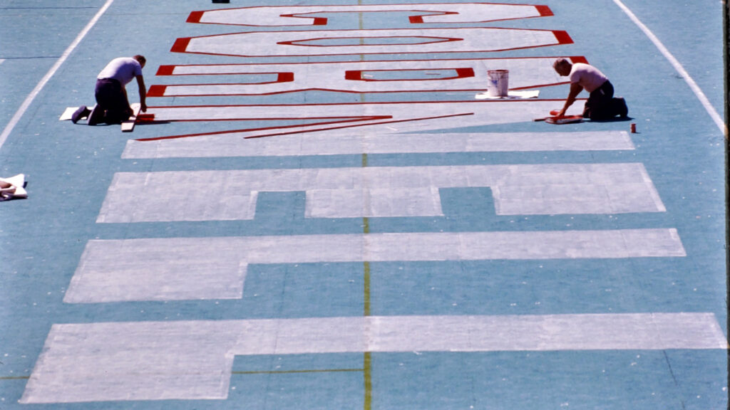 workers paint a red outline around large white letters spelling "CORNELL" in Schoellkopf Stadium, 1977