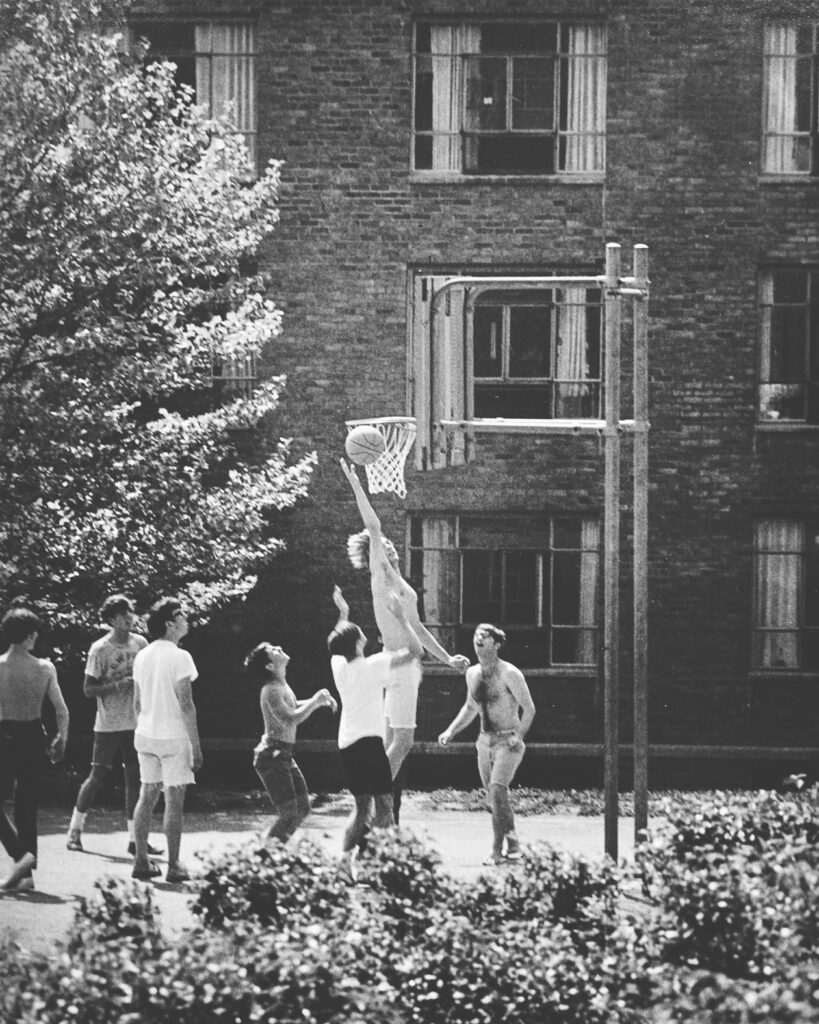 Students play basketball on a court outside one of the University Halls, late 1970s or early 1980s.