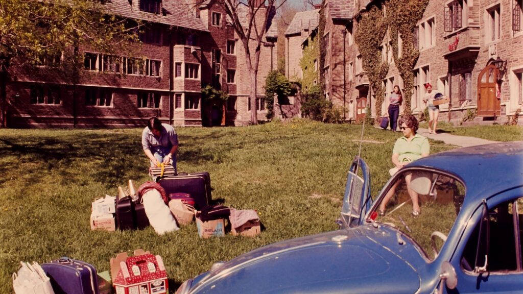 a campus scene as students move out of residence halls with a Volkswagen Beetle in the foreground, 1972