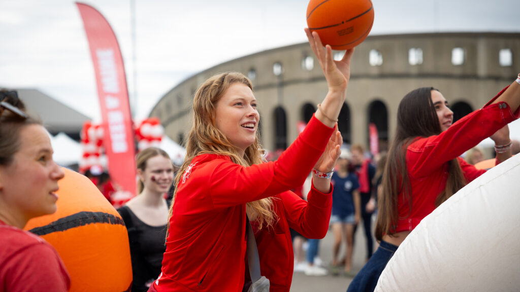 an attendee tries her hand at a basketball toss game at the Big Red Fan Festival during Homecoming 2024