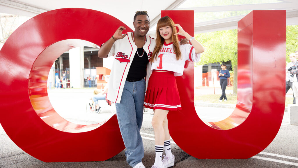 two Cornellians pose in front of the "CU" letters at the Big Red Fan Festival during Homecoming 2024