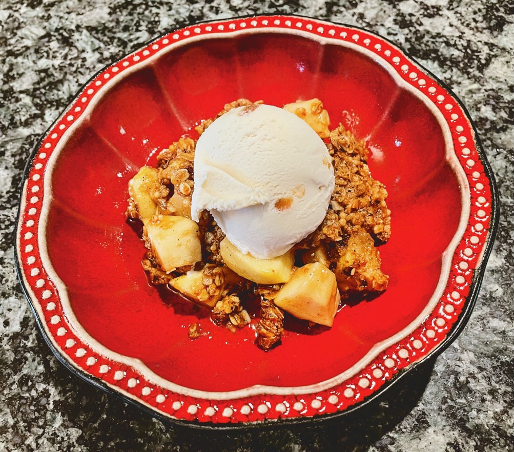 A serving of apple cobbler with ice cream in a red dish