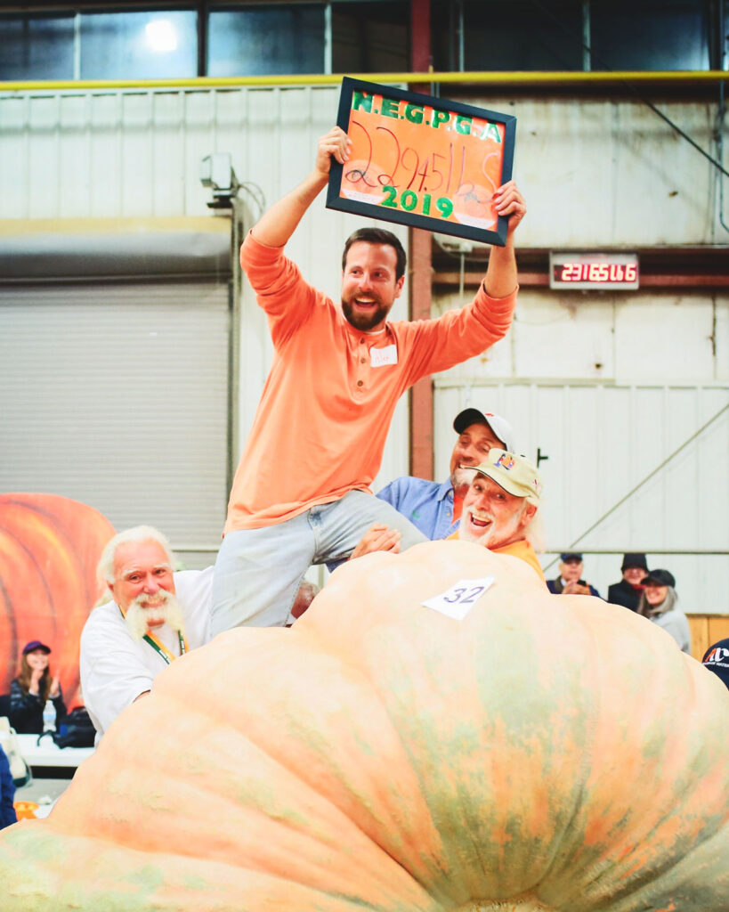 Alex Noel holds a sign up displaying his giant pumpkins weight, 2,294.5 pounds, while being held up by fellow giant pumpkin growers at a weigh-in.