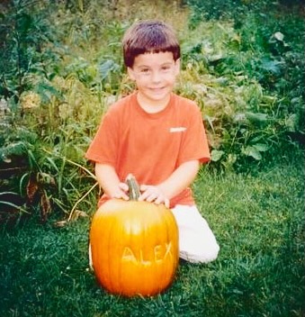 Alex Noel as a young boy smiles with a pumpkin with his name carved into it.