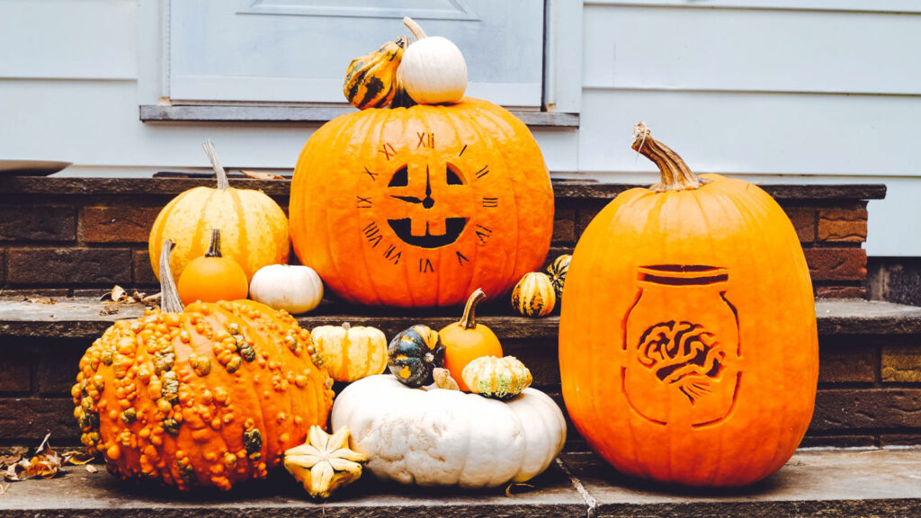 two carved pumpkins with other gourds displayed on outdoor steps