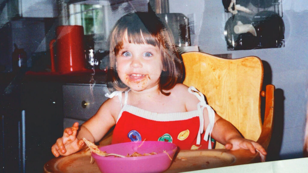 Kristin Stinavage as a toddler eating spaghetti in a high chair