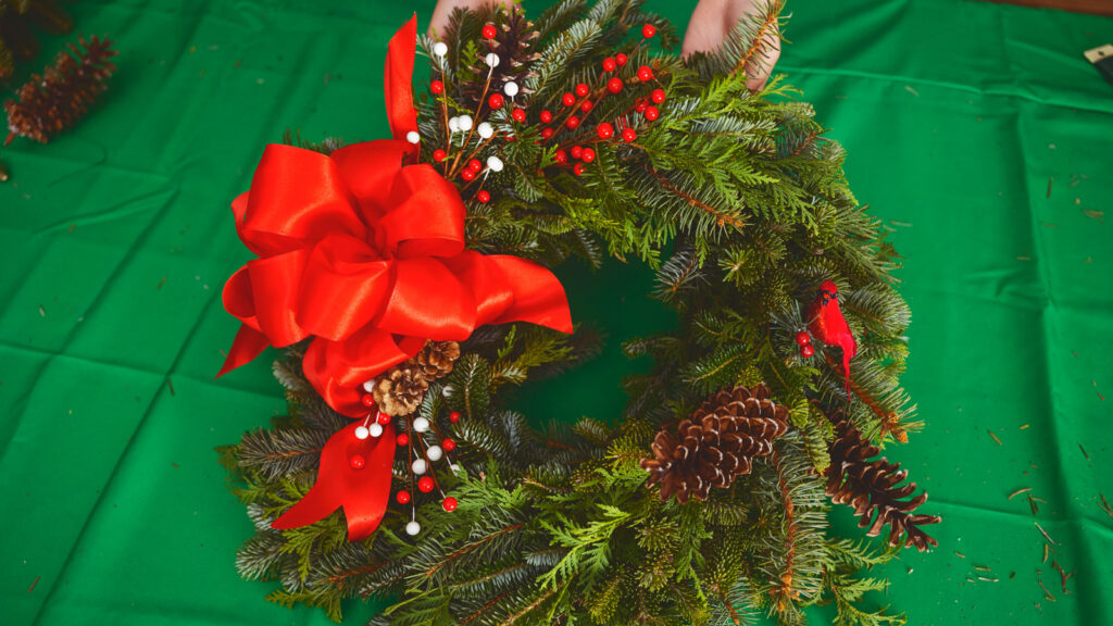 A completed wreath with pinecones, berries, and a big red bow.