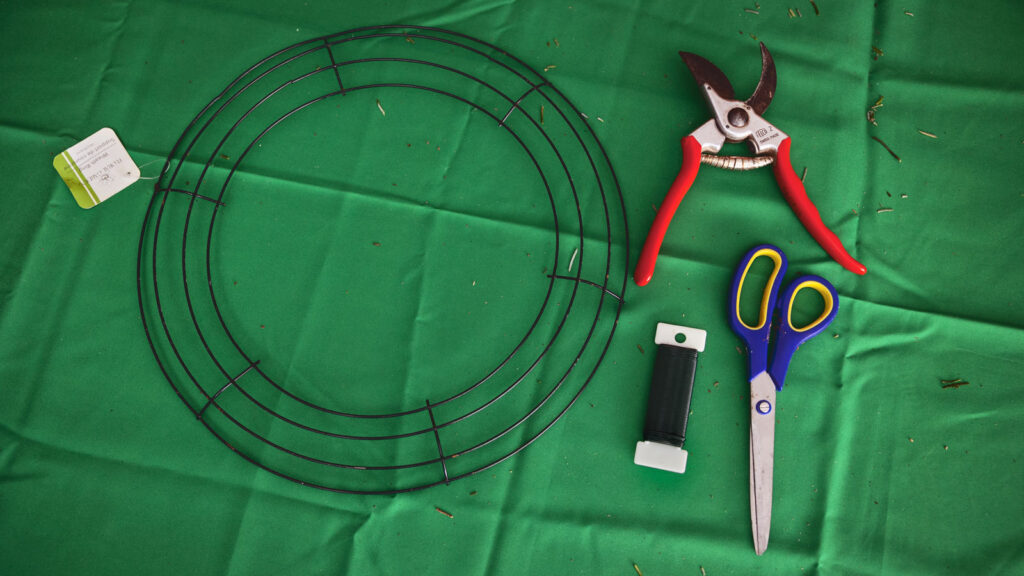 All of the tools that and materials that are needed to make a wreath: a wreath frame, clippers, scissors, and wire.