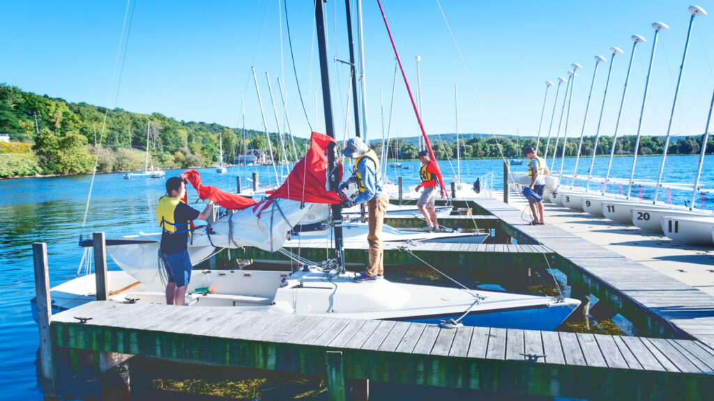 students and sailing personnel take down sails after docking