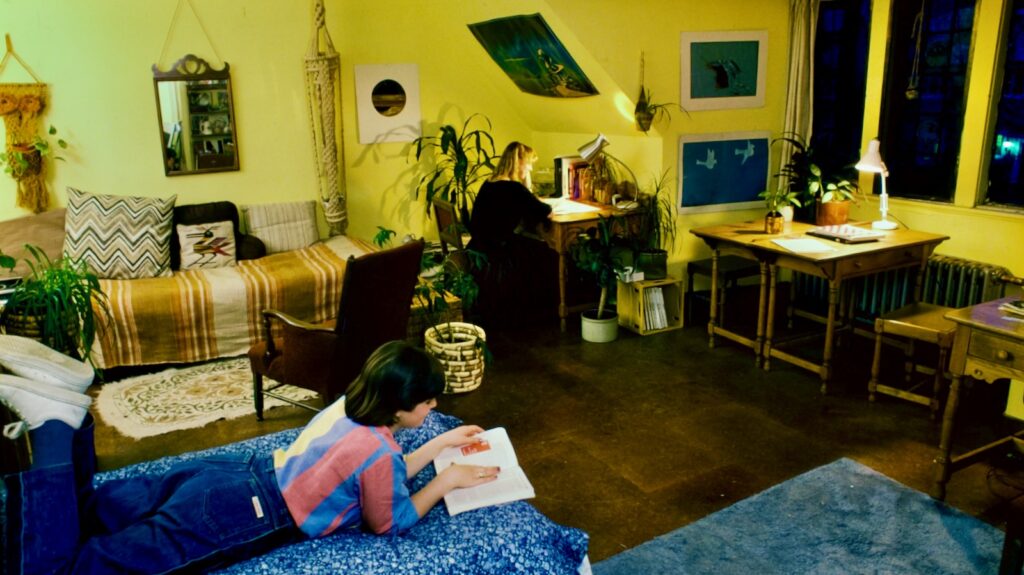 Two students relax in a dorm room with a sloped ceiling, 1984