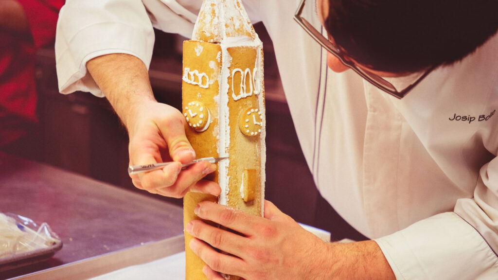 Joe Boko, executive chef at the Cornell Club-NYC, cleans up edges of royal icing on the gingerbread McGraw Tower in the club kitchen