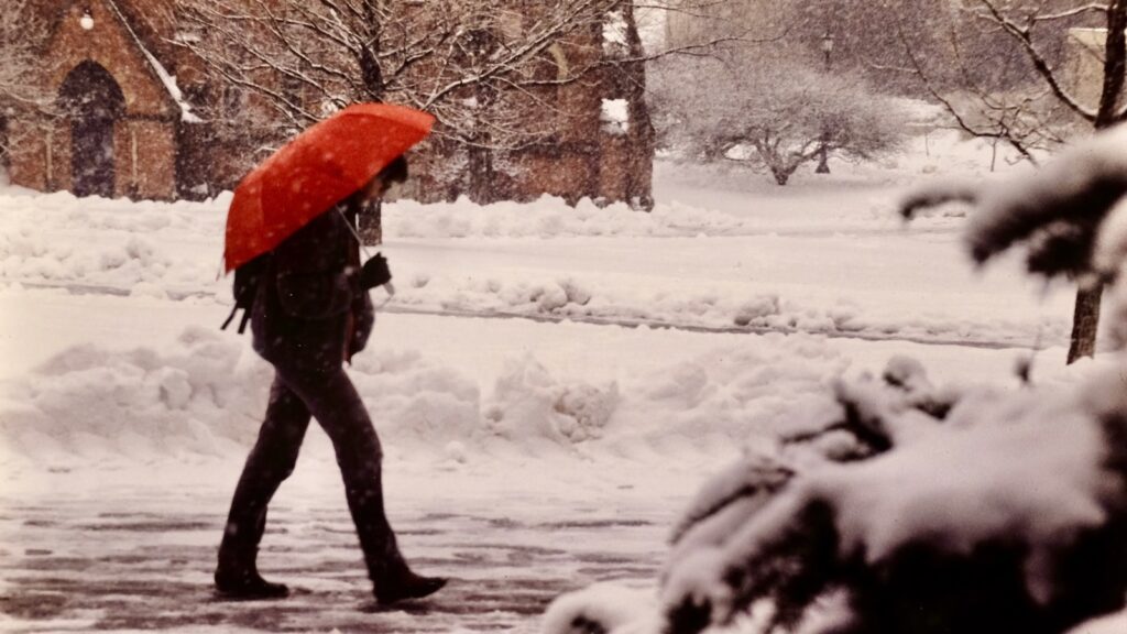 a pedestrian with a red umbrella crosses near Sage Chapel in the snow in 1983