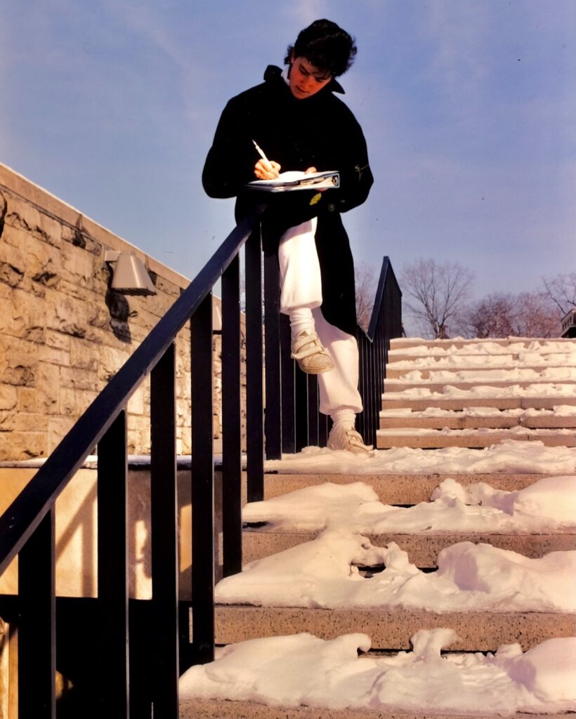 a student sits on a stairway railing amid snow-covered steps by Olin Library in 1984