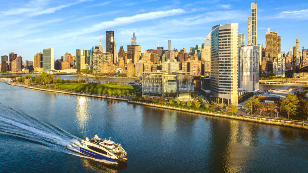 aerial view of the Cornell Tech campus on Roosevelt Island, looking southwest with Manhattan’s east side, the East River, and a passing boat visible