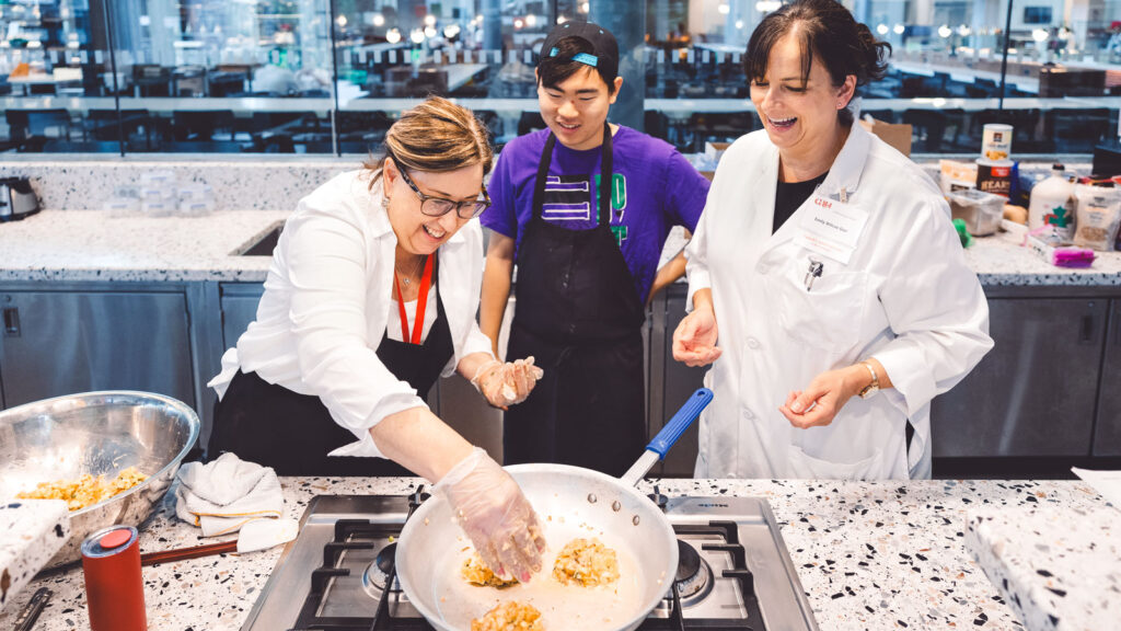 Two women and a man cooking over a stove and smiling