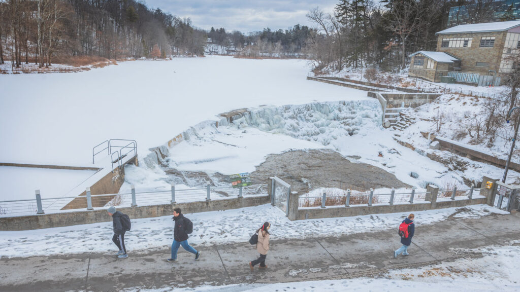 Students walk on the Triphammer Falls footbridge near Beebe Lake