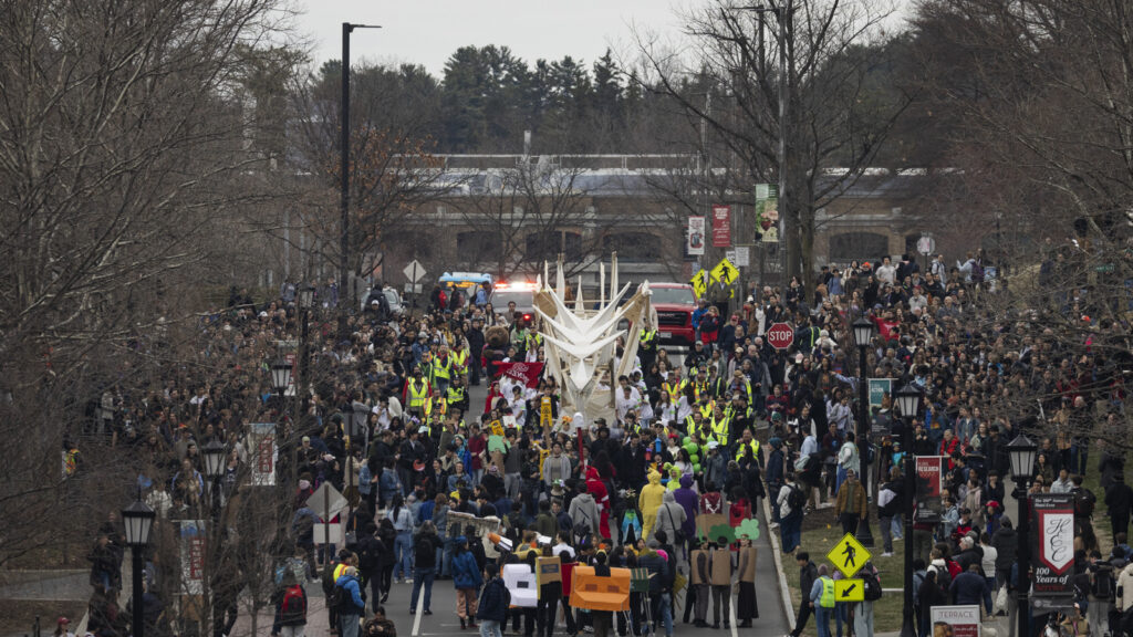 the dragon, flanked by students and spectators, heads down Feeney Way during Dragon Day 2025