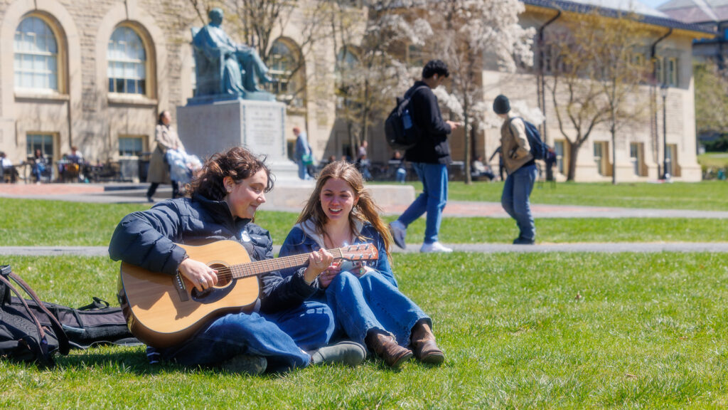 A student plays guitar sitting in the Arts Squad with another student