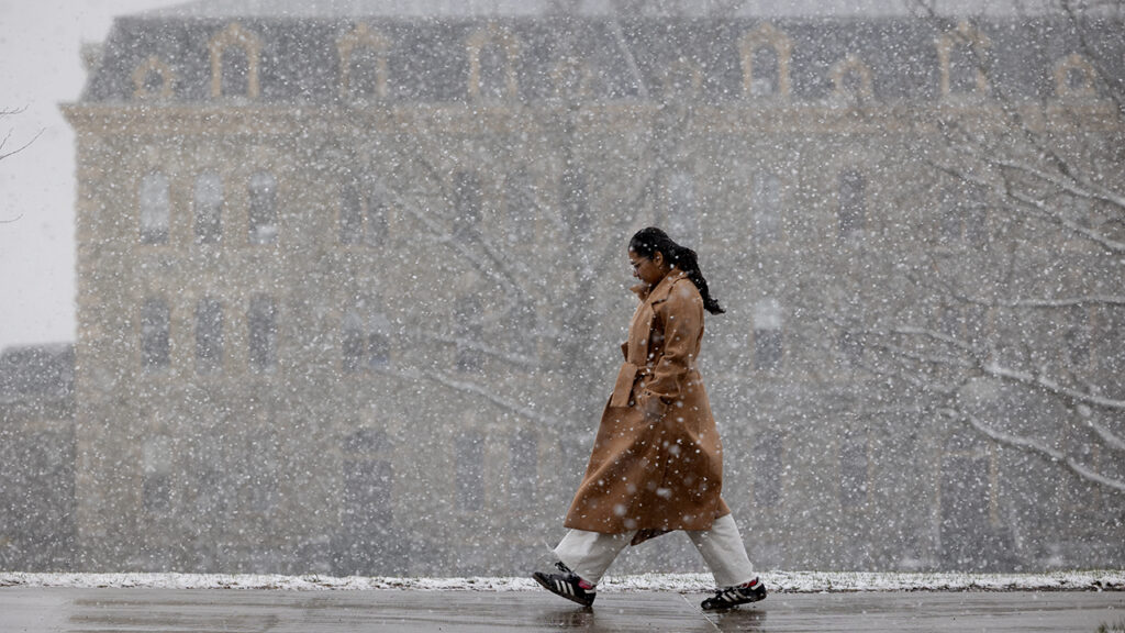 Spring snow falls outside White Hall as a woman walks by