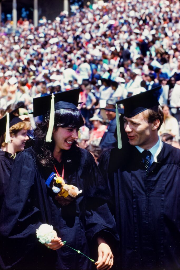 Two grads wearing cap and gown holding a flower