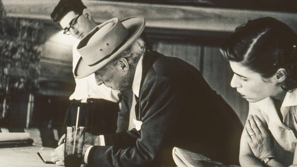 Frank Lloyd Wright, center, sketches a design in the Reisley home as Roland and Ronny Reisley look on
