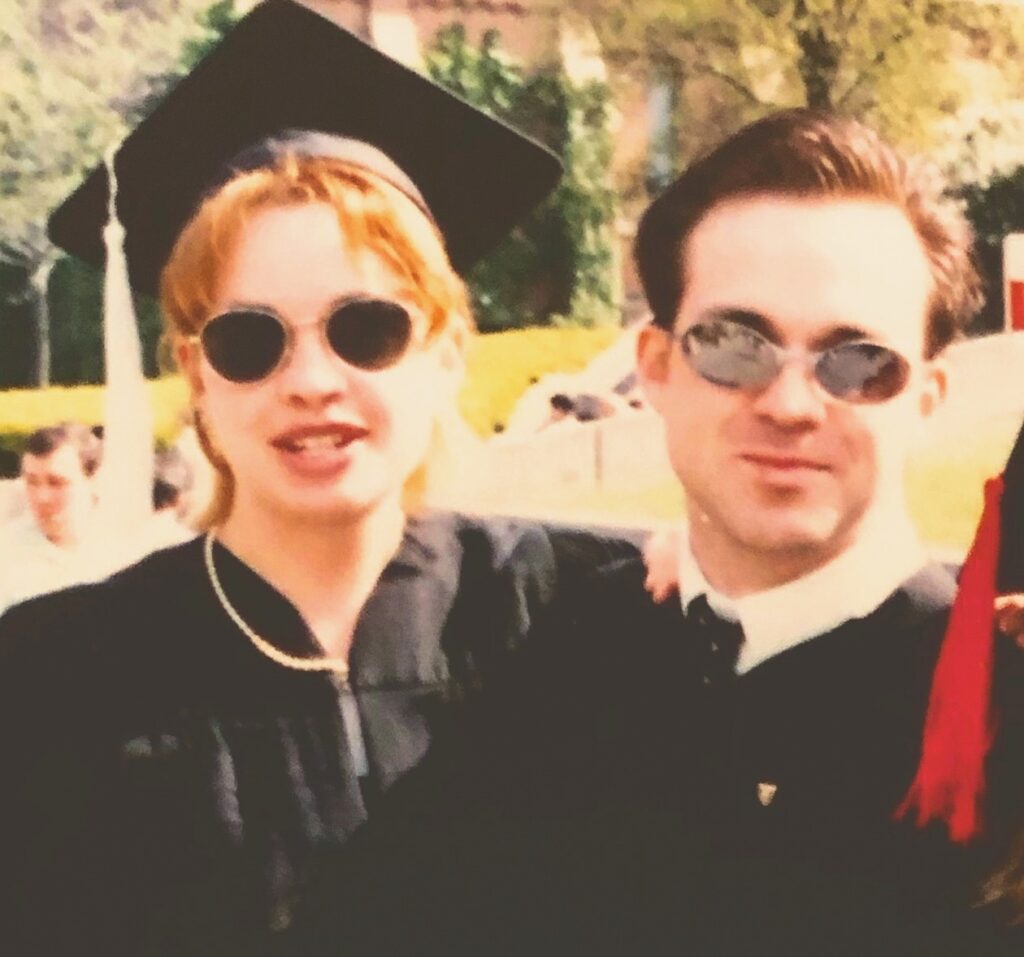 Jessica O'Toole in her graduation cap and gown on campus with her husband Jess Mullen-Carey, also in gown.