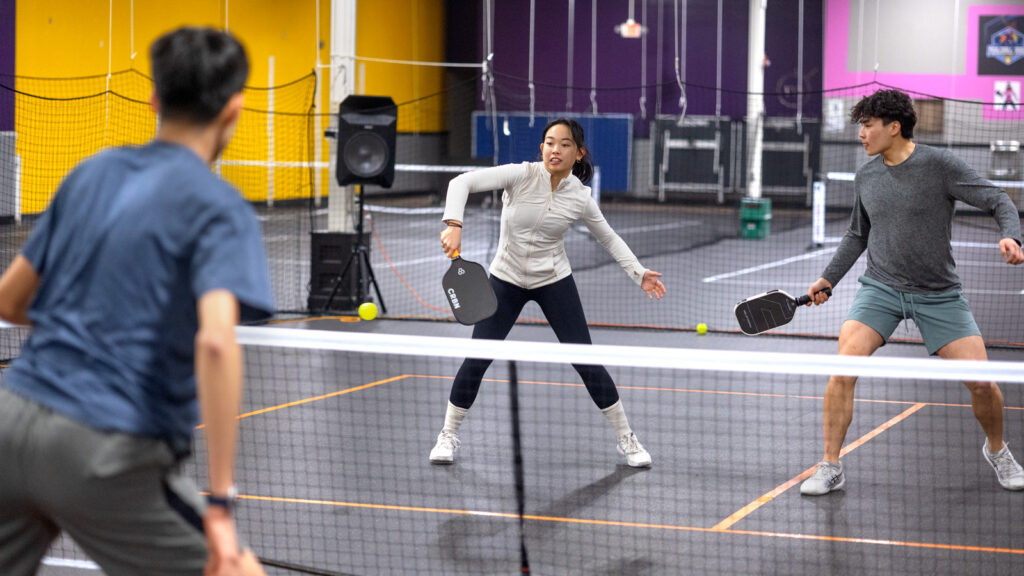 Three students in athletic clothing play pickleball together.